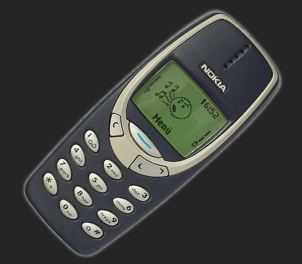 Zdjęcie pokazujące stary telefon komórkowy, Nokię 3310, z fizycznymi klawiszami oraz emotką wyświetloną na ekranie